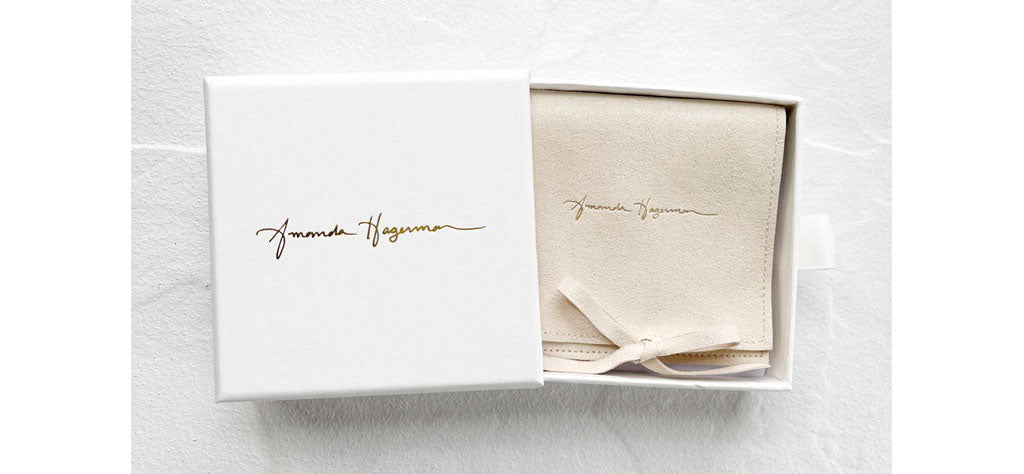 White jewelry box with gold embossed Amanda Hagerman logo and off-white jewelry pouch